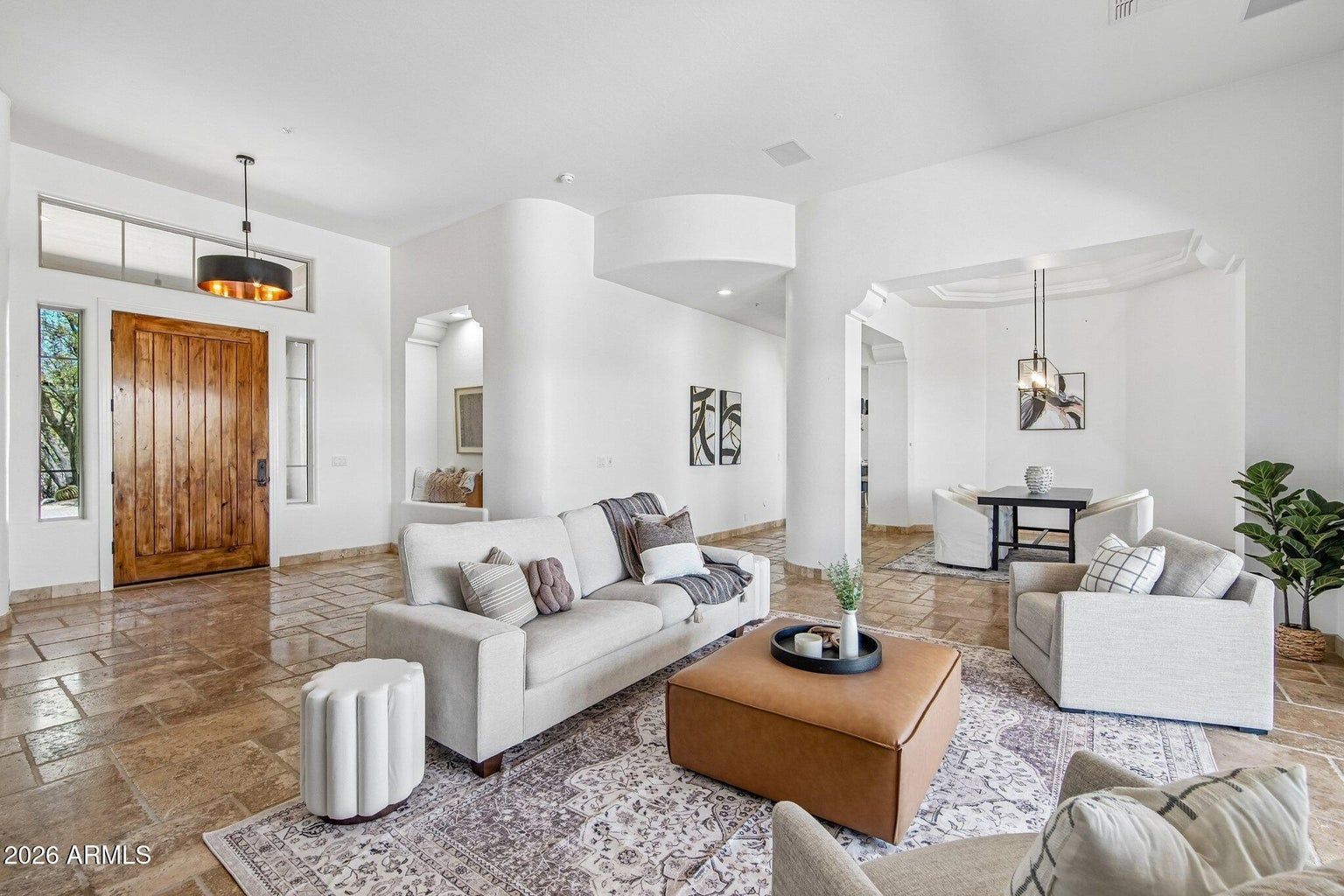 Bright modern living room with white walls, beige sofas, patterned rug, and wood front door.