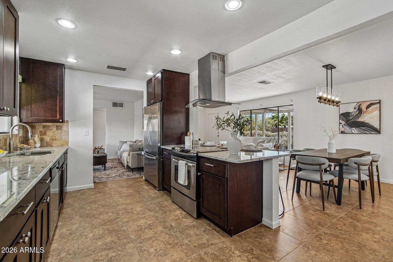 Modern kitchen with dark wood cabinets, stainless appliances, and a dining table beside an open living area.