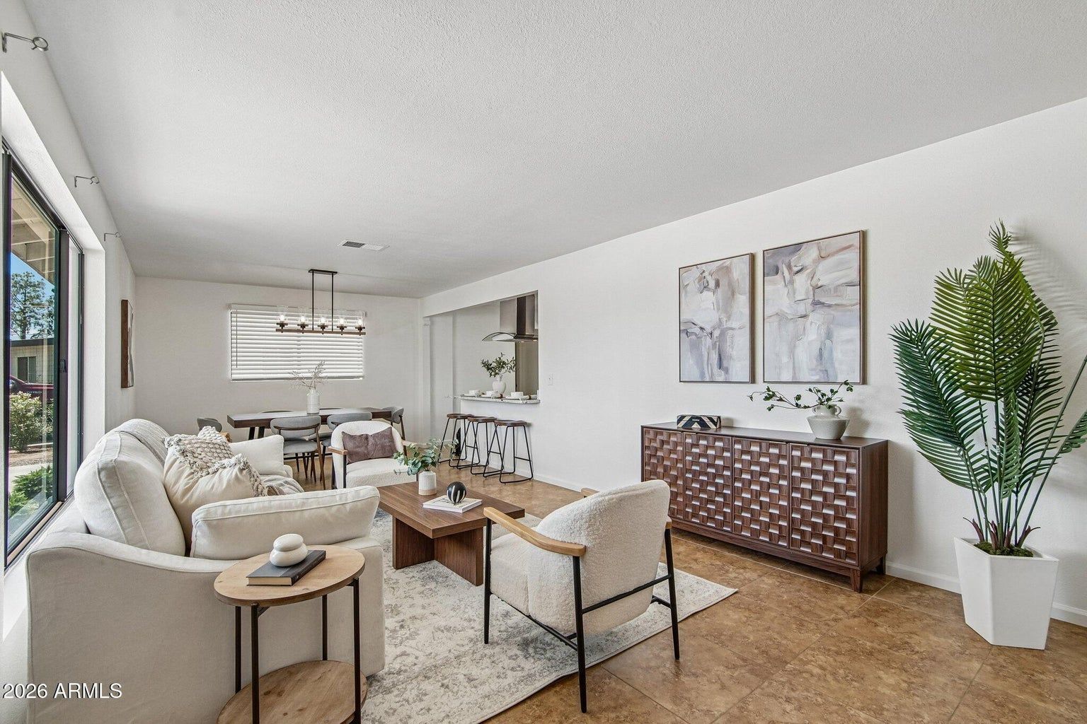 Bright, airy living room with beige sofas, wood furniture, wall art, and a potted plant.