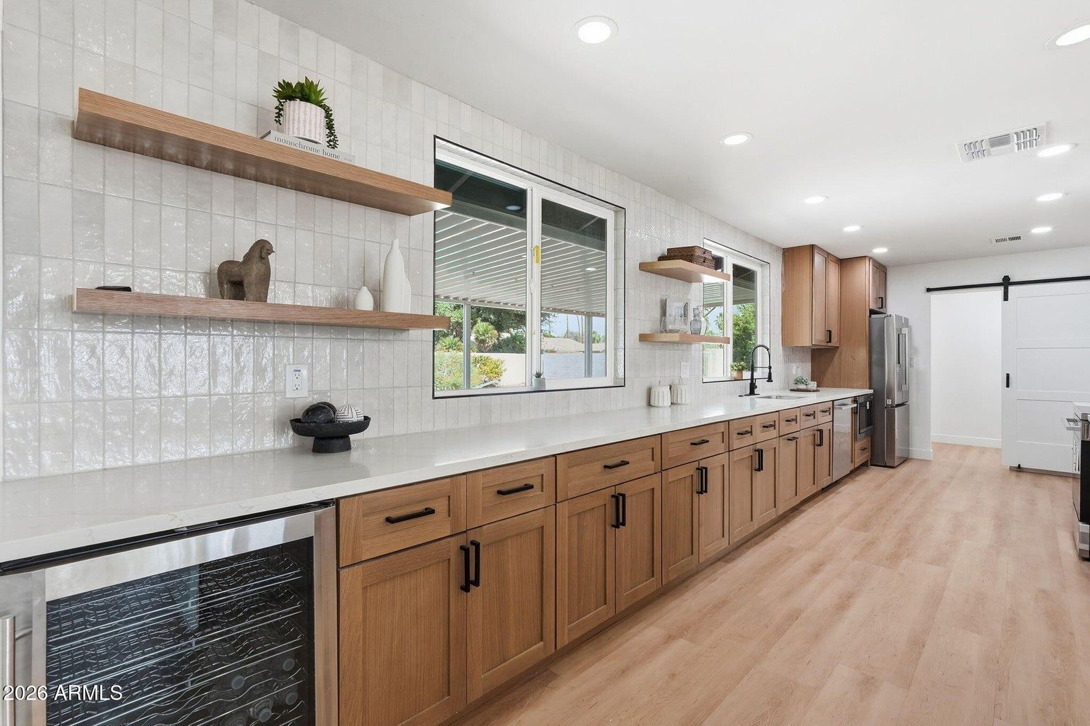 Bright modern kitchen with wood cabinets, white countertops, open shelves, and a windowed sink area.