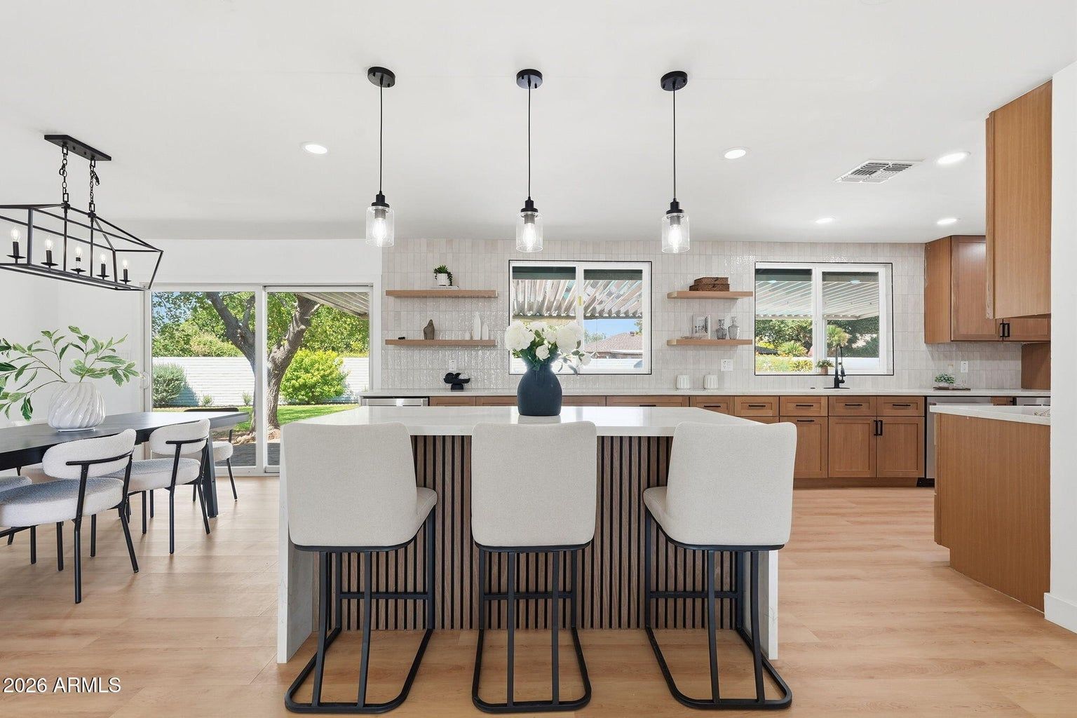 Bright modern kitchen with island, bar stools, pendant lights, and dining area with large windows.