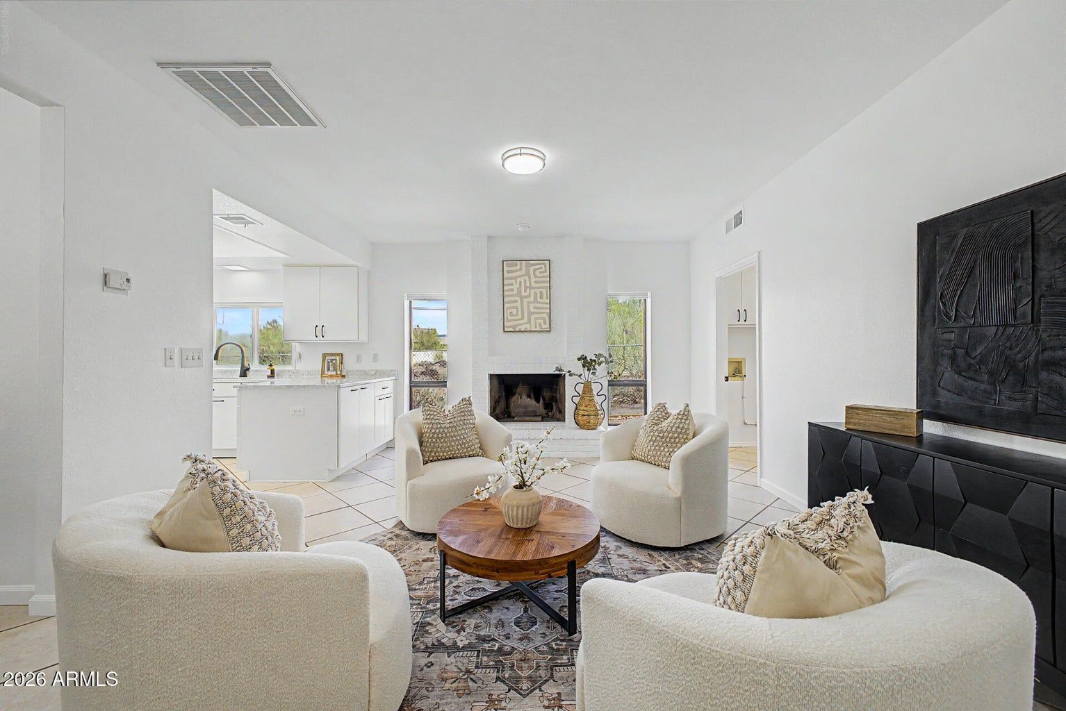 Bright white living room with round chairs, coffee table, fireplace, and kitchen in the background.