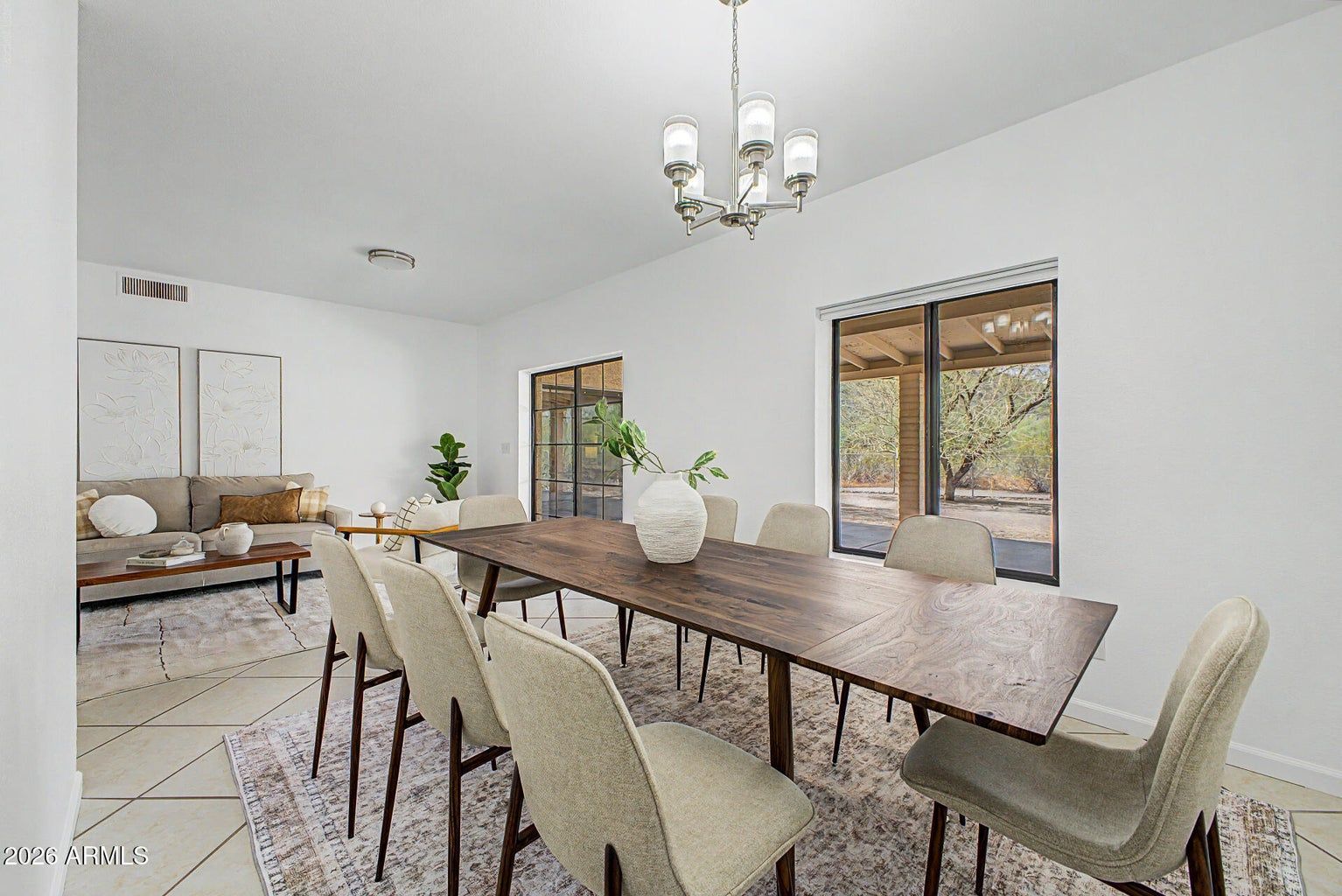 Bright dining room with long wood table, beige chairs, chandelier, and large windows.