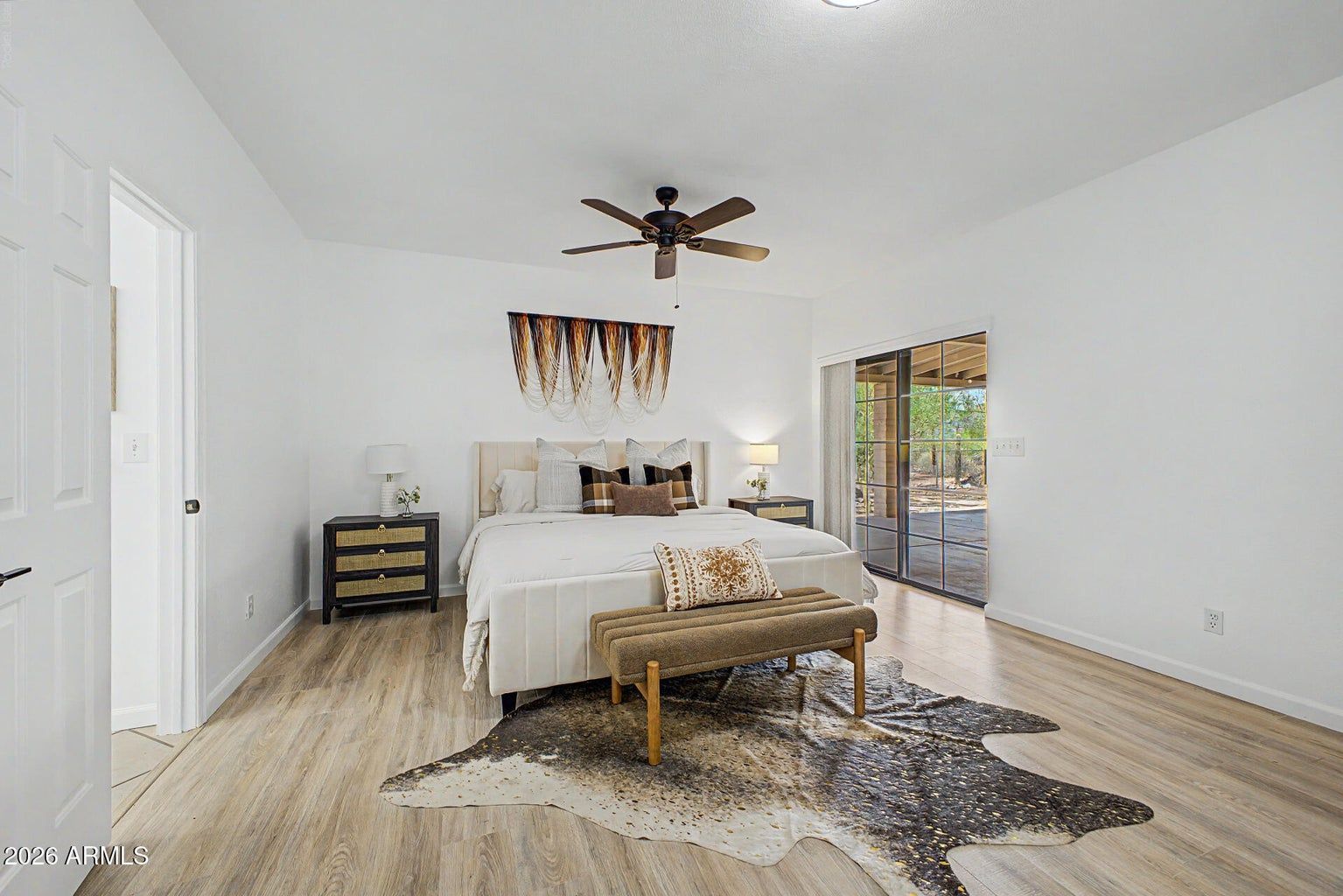 Bright bedroom with white walls, queen bed, bench, ceiling fan, and sliding doors to a patio.