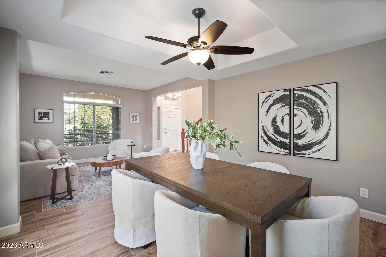 Bright dining room with a dark wood table, white chairs, ceiling fan, and abstract wall art.