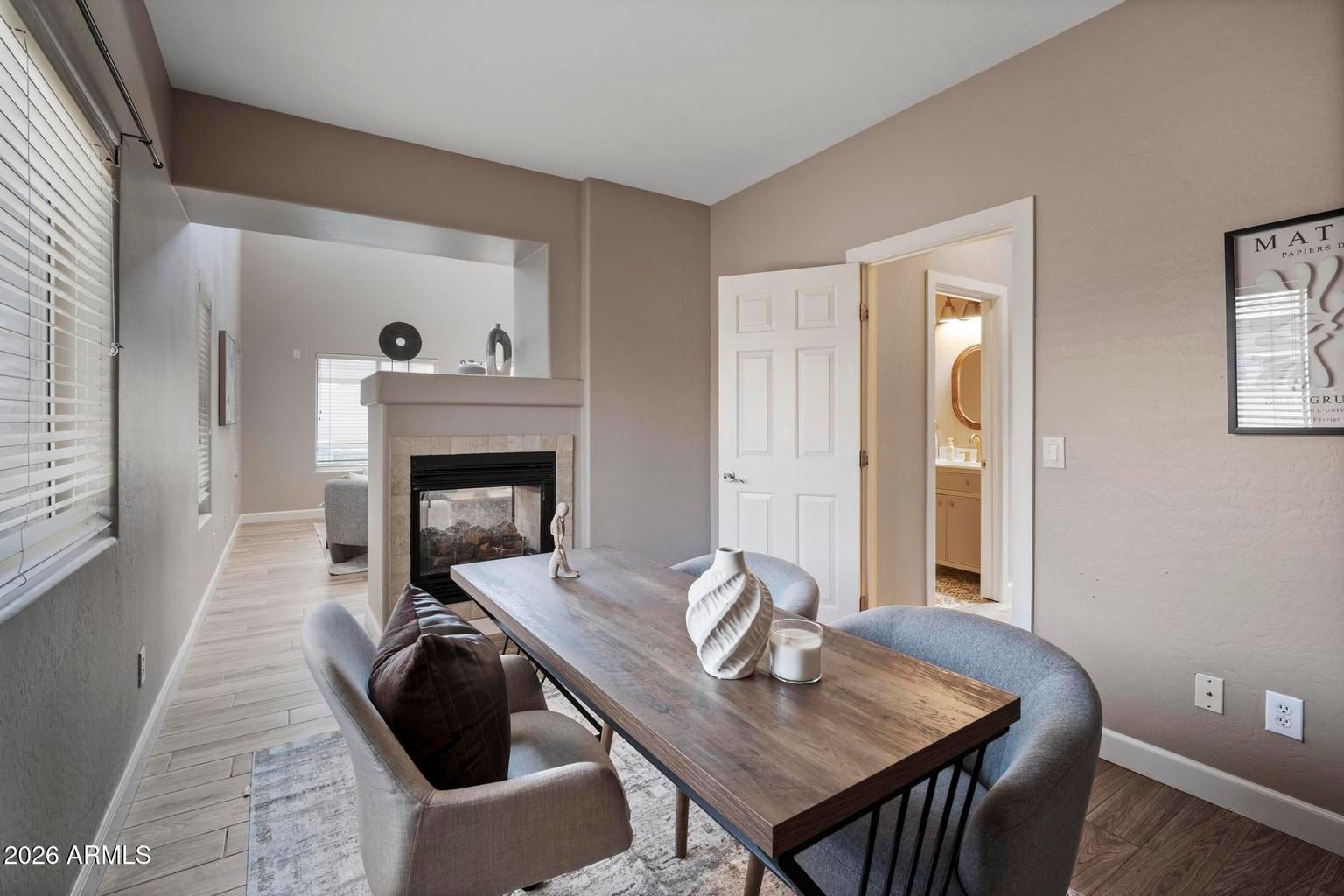 Modern dining room with wood table, gray chairs, fireplace, and open doorway to a bright bathroom.