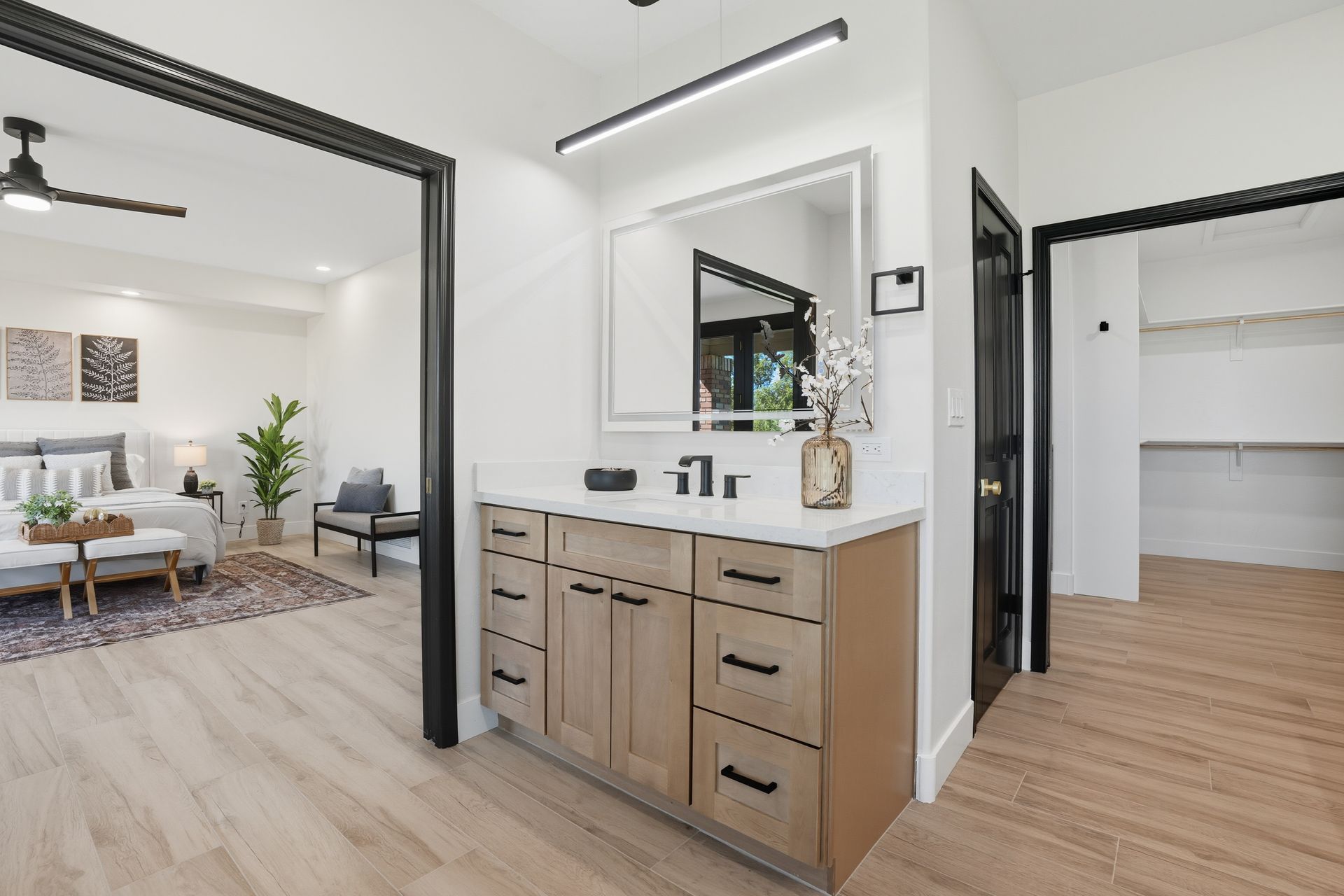 Modern bathroom with double vanity, wood cabinets, black-framed mirror, and open doorway to a bedroom.