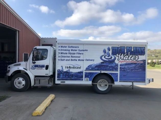 A white service truck for High Plains Water parked outside a metal building on a sunny day.
