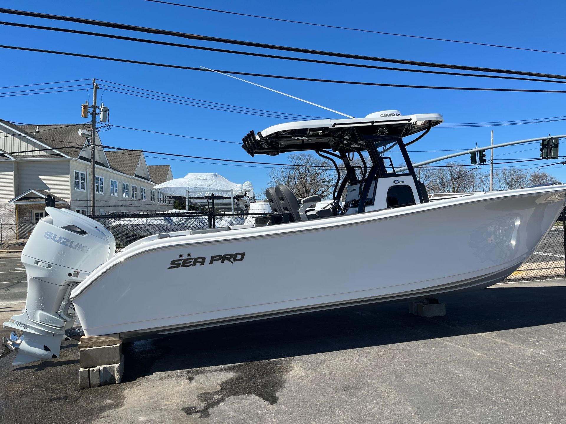 A white Sea Pro center console boat with a T-top on cinder block supports in a parking lot under a clear blue sky.