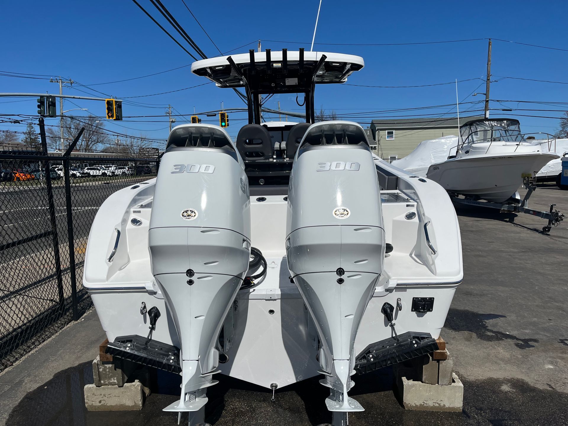 Rear view of a white center console boat with dual outboard motors parked on concrete blocks in a parking lot.
