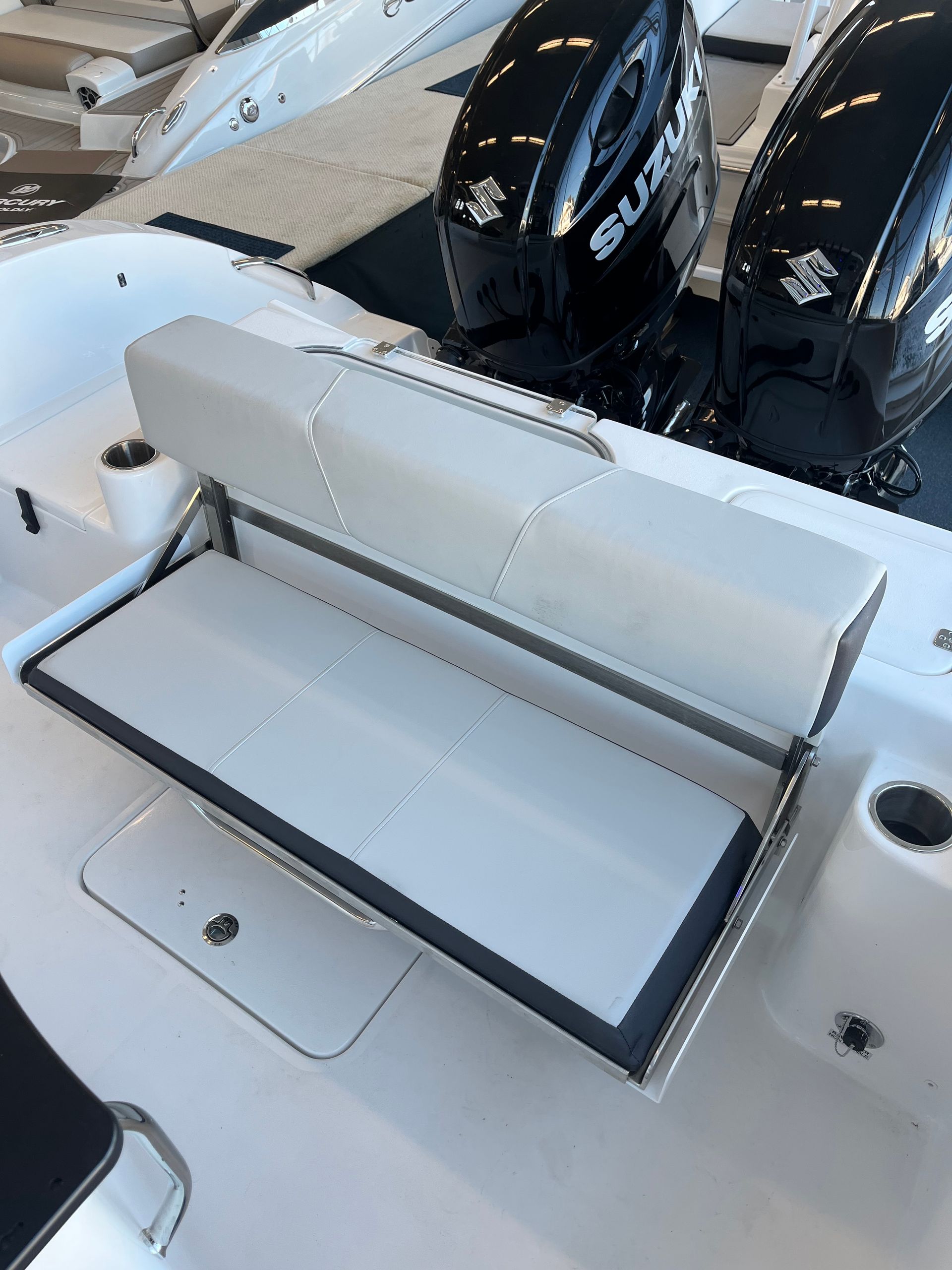 White boat with fold down seat, two black Suzuki outboard motors in the background.