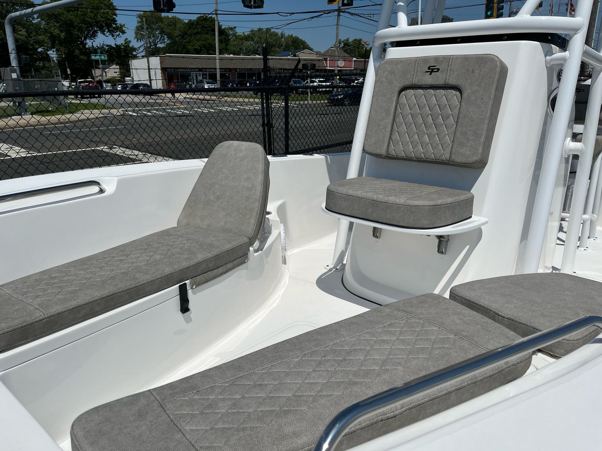 A white boat with gray seats is parked in front of a chain link fence.