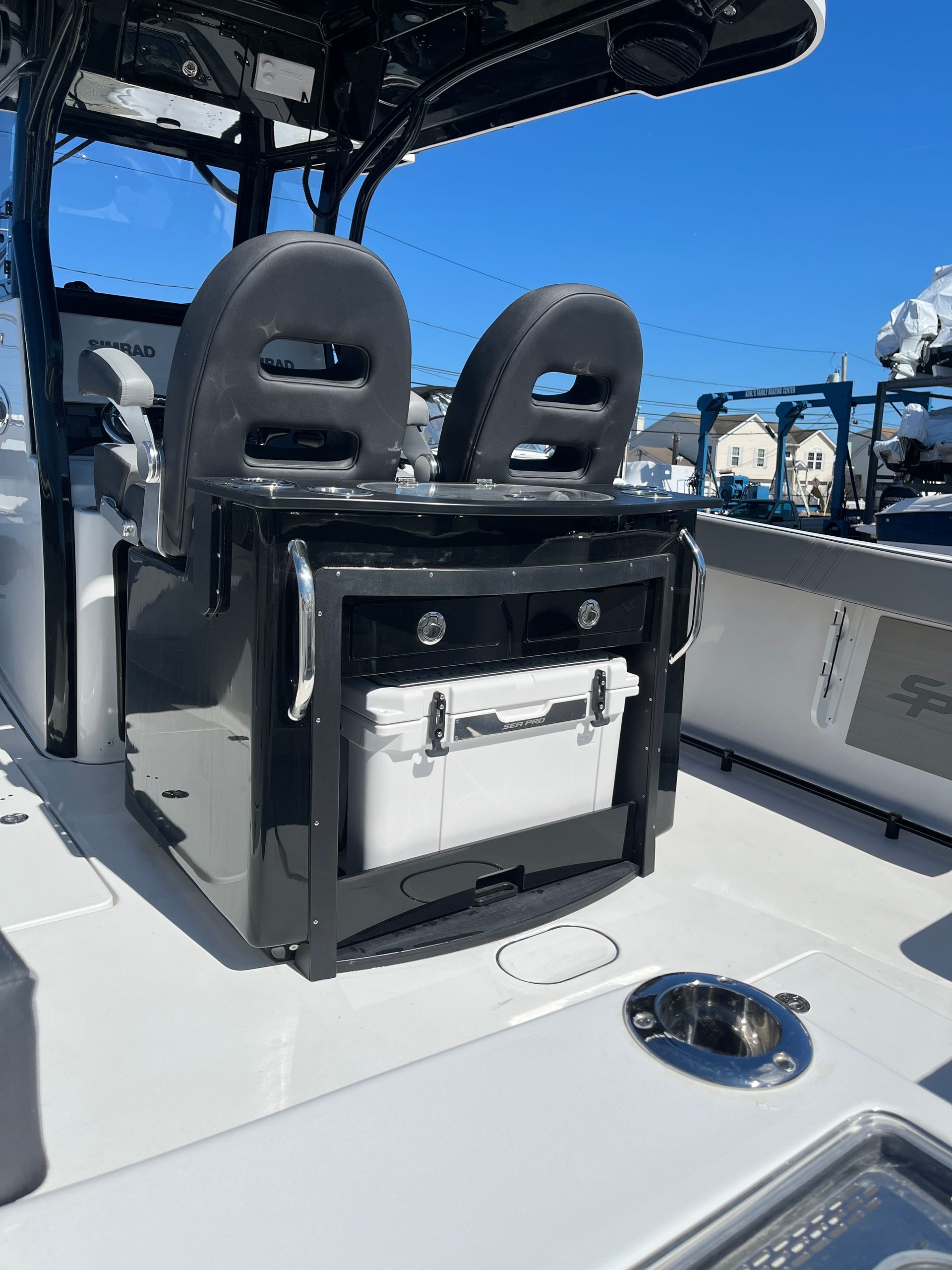 A white boat deck featuring a black captain's chair console with two grey seats and a slide-out white cooler beneath.