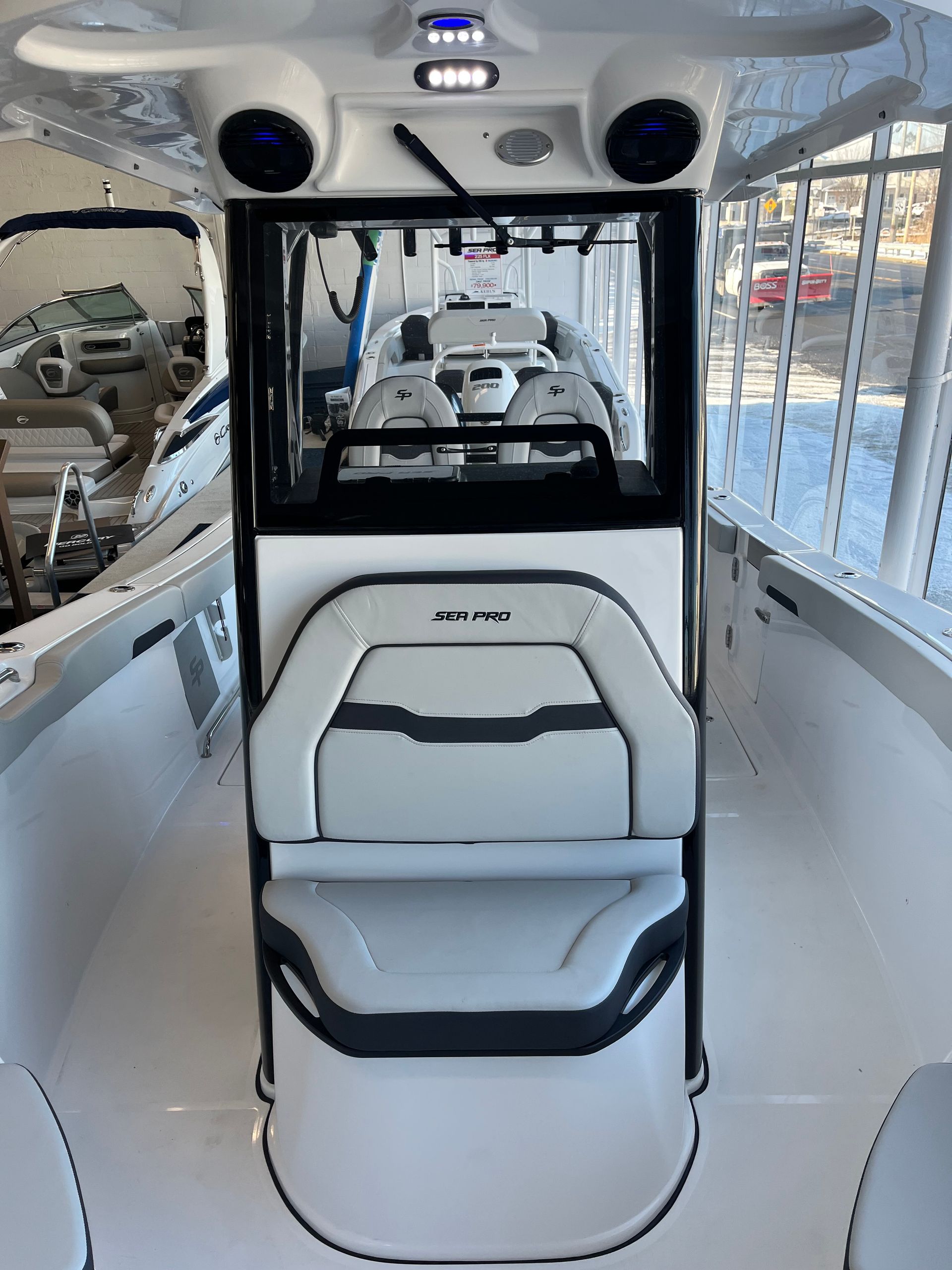 Interior view of a boat cockpit with white and gray seats, control panel, and overhead speakers.