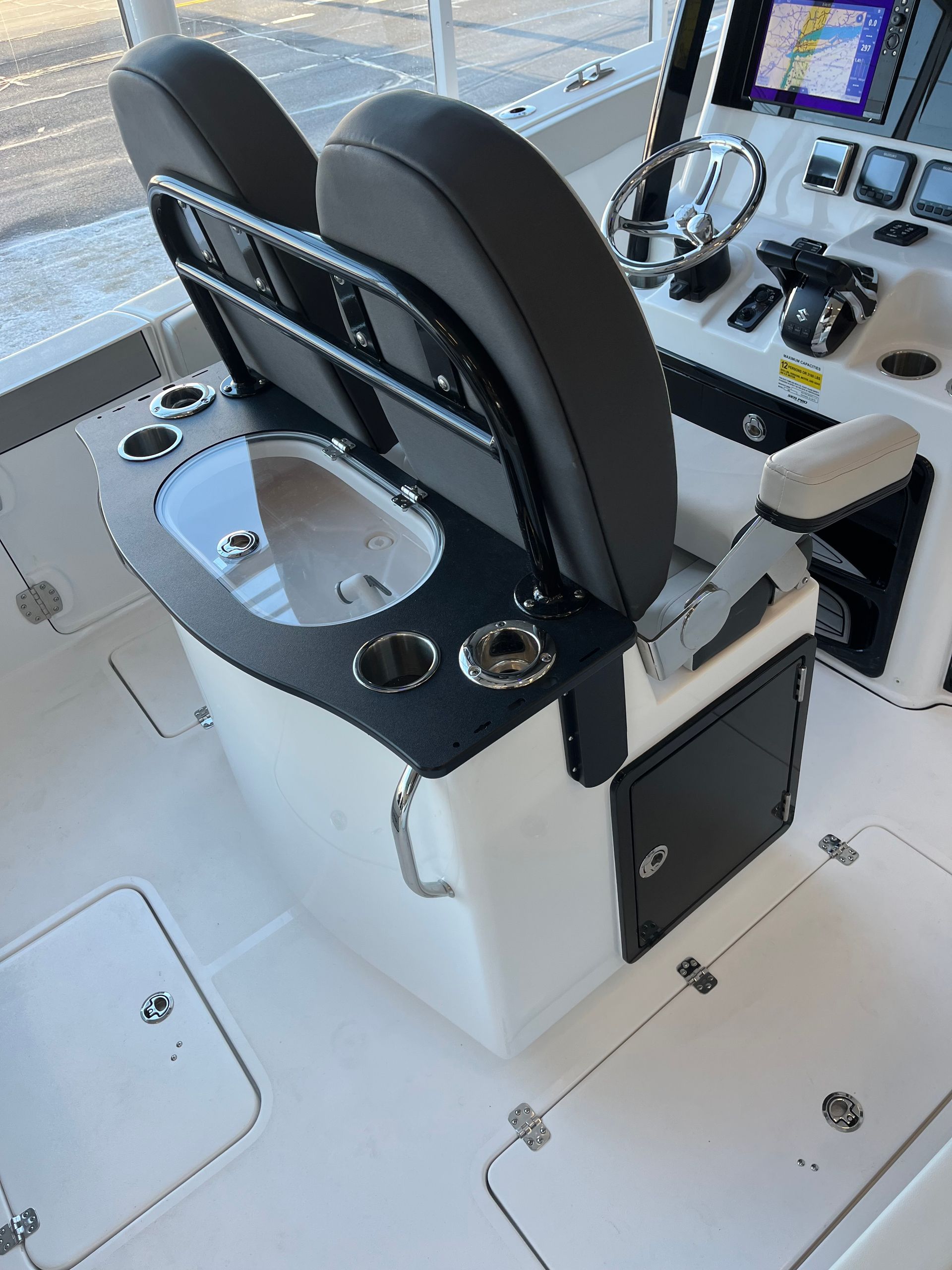 Boat cockpit with two black seats, steering wheel, console with cup holders, and a small sink.