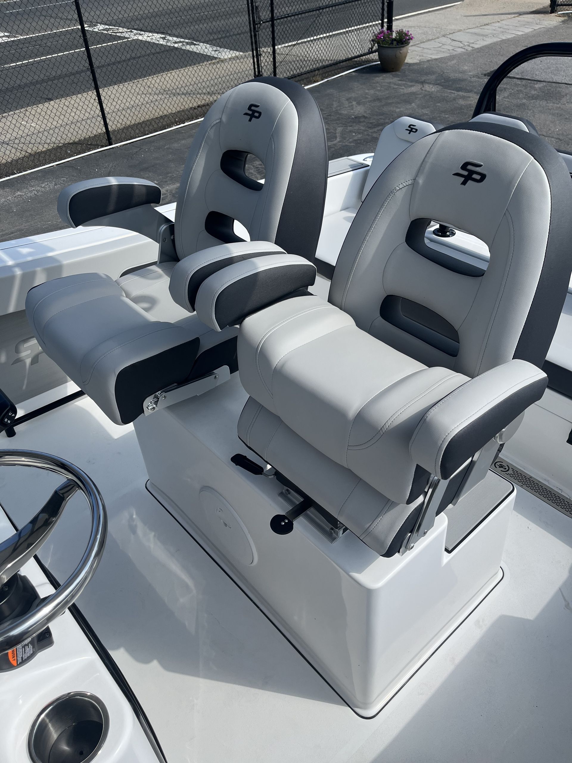 Two gray boat seats on a white boat with a steering wheel and cup holder visible.