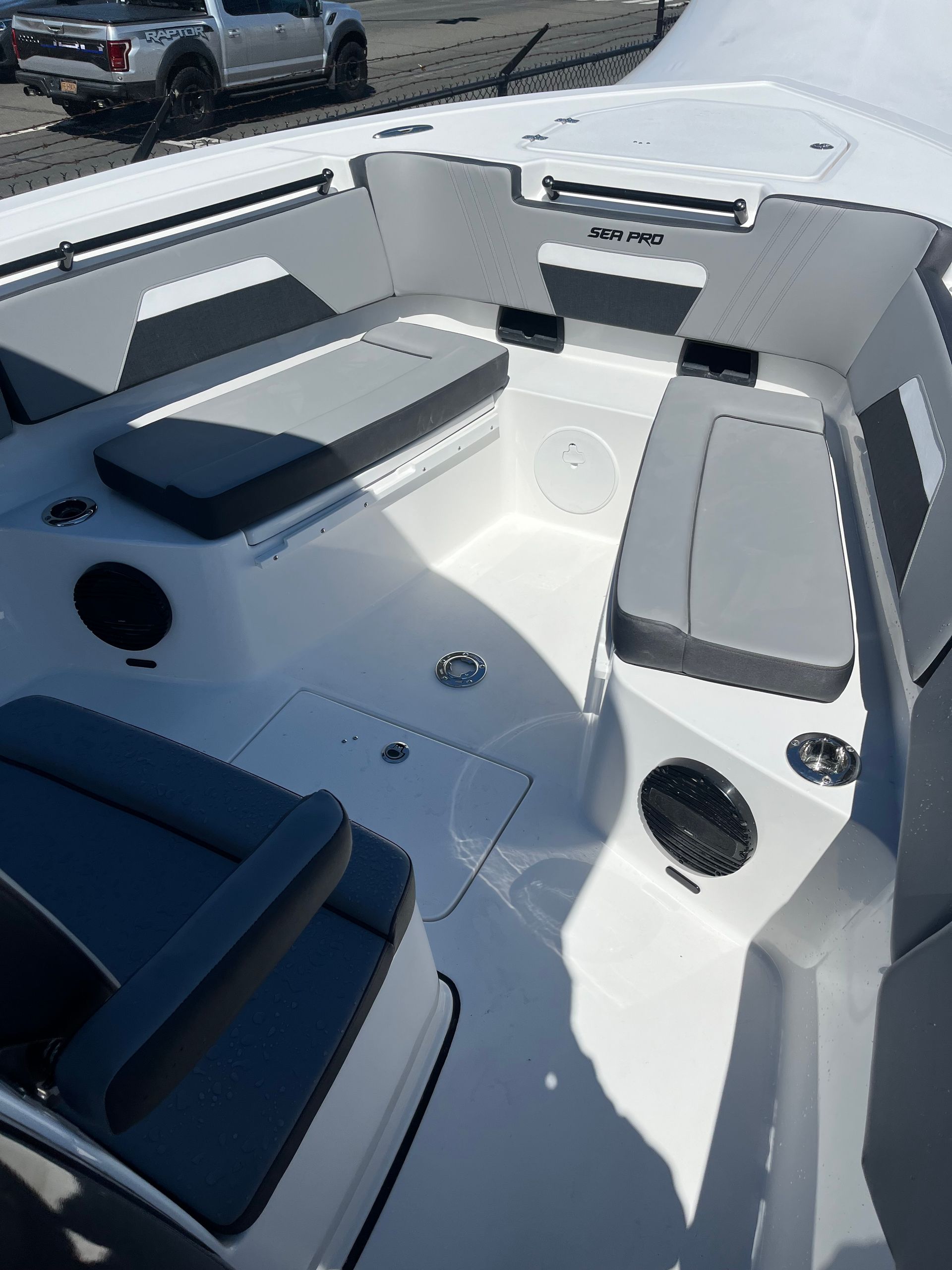 Interior view of a white boat deck with gray cushioned benches, dark speakers, and a white fiberglass finish.