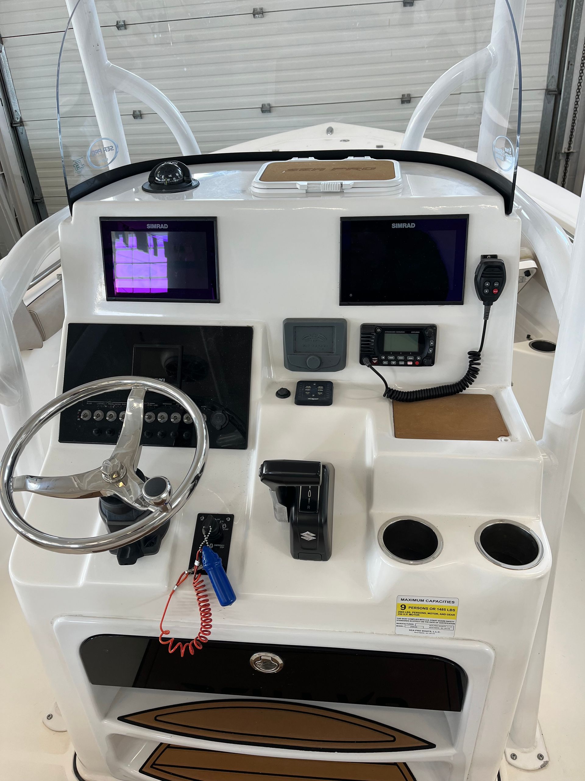White boat dashboard with navigation screens, steering wheel, radio, and cup holders.