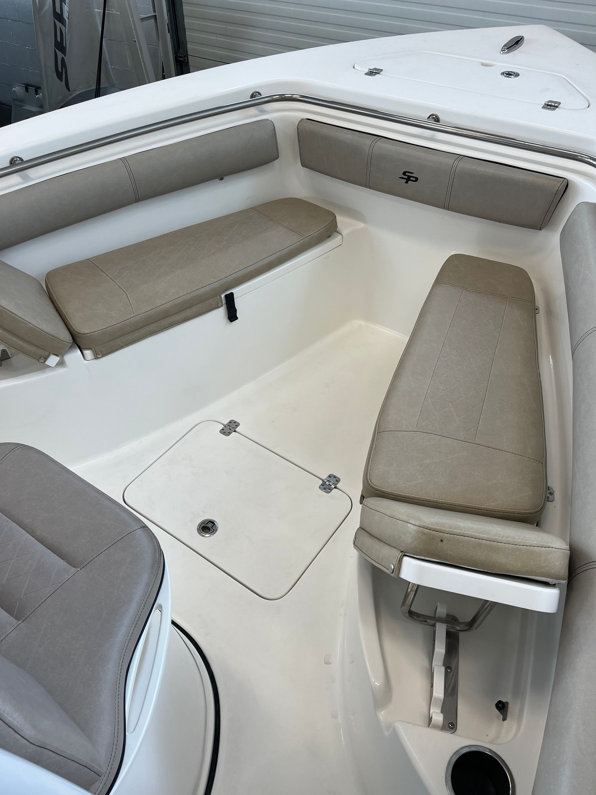 Interior of a boat with beige upholstered seats, white flooring, and metal railings.