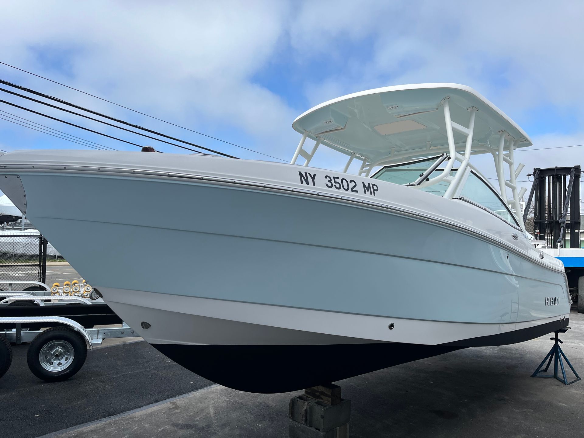 White cabin boat on a trailer at a marina, with blue sky and dock equipment in the background