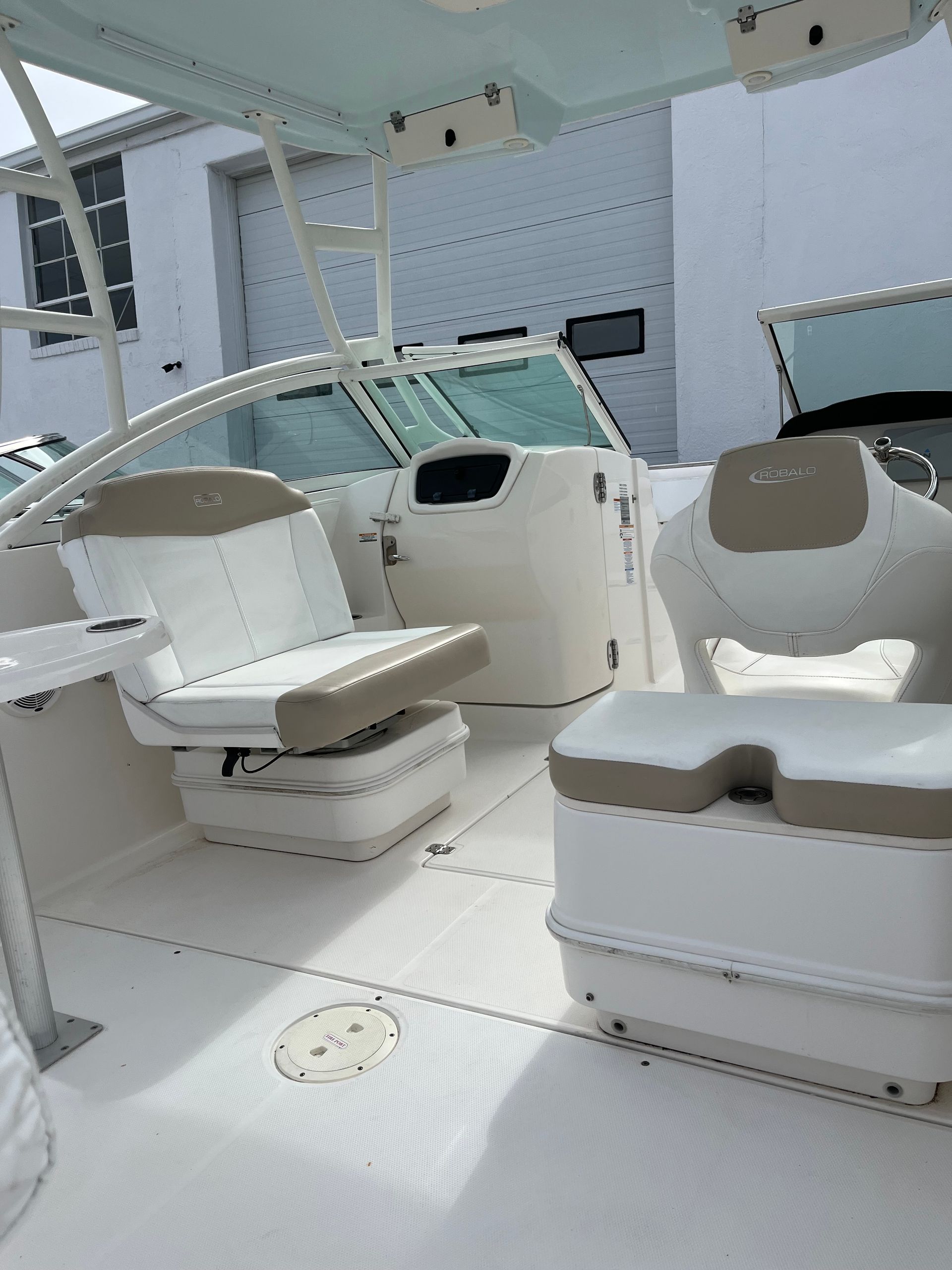 White boat cockpit with cream seats and helm under a canopy, docked beside a building.