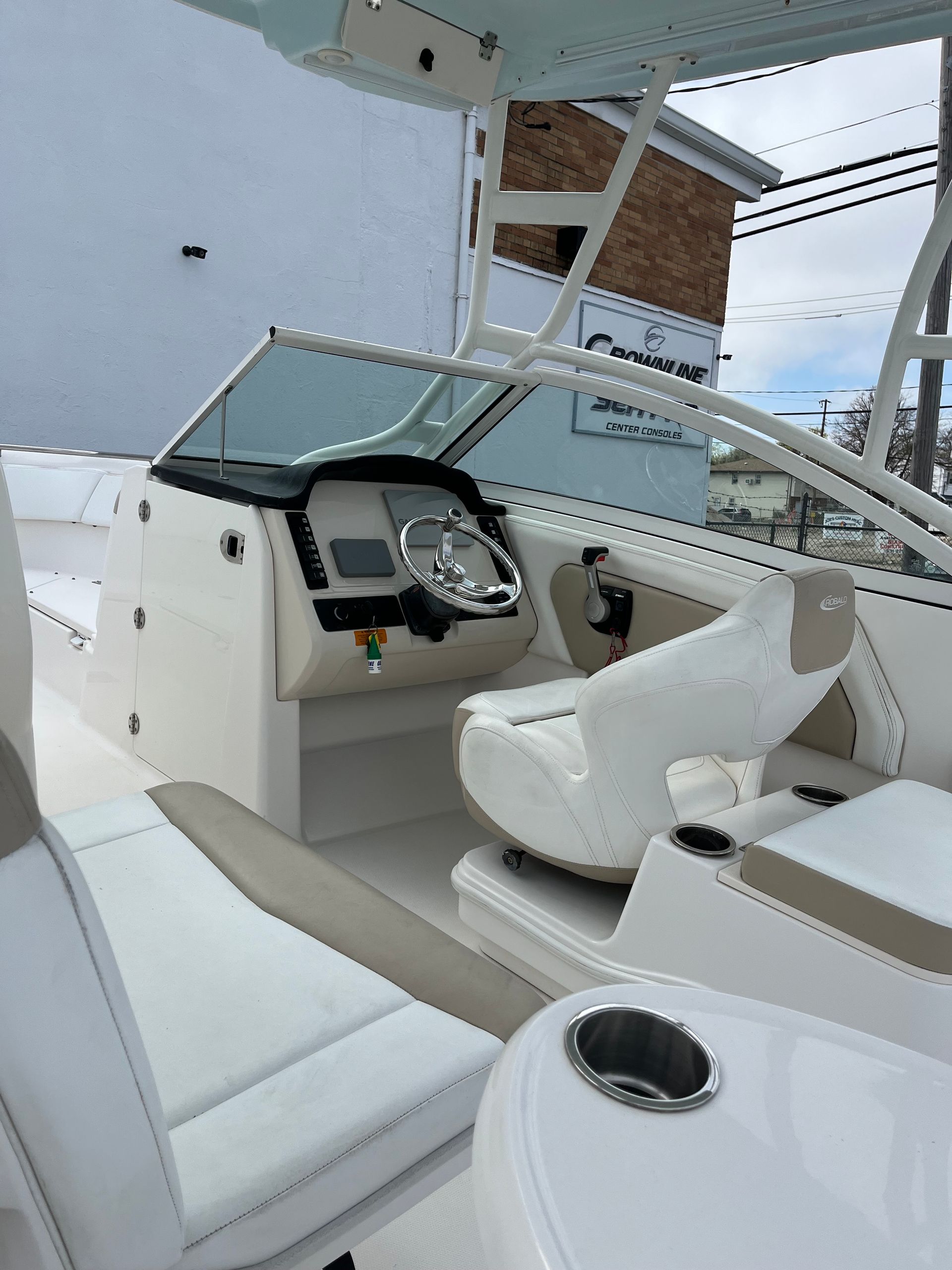 Boat cockpit with white seats, steering wheel, and windshield on a docked vessel.