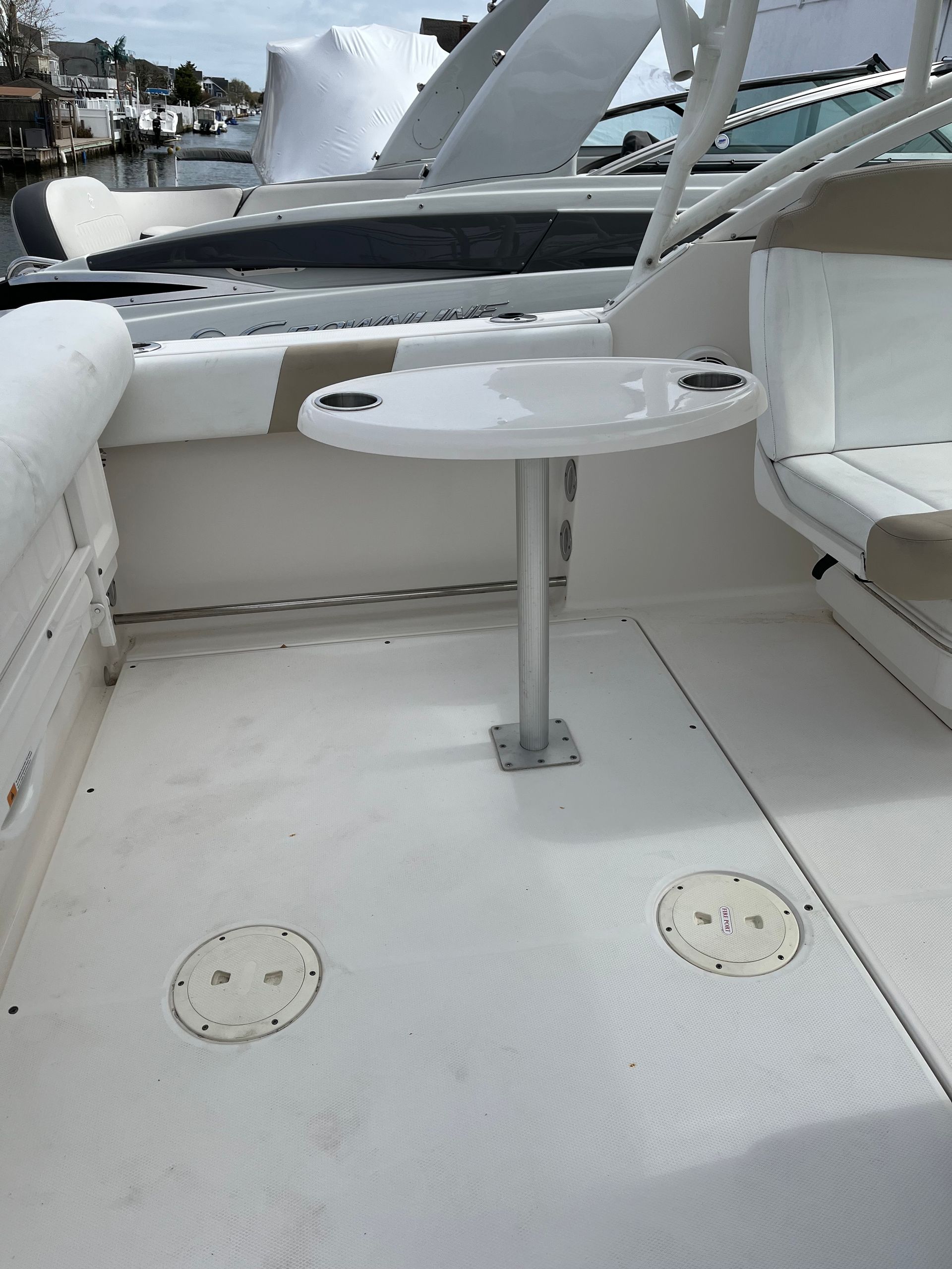 White boat cockpit with a small round table and cushioned bench seats, water and dock visible beyond