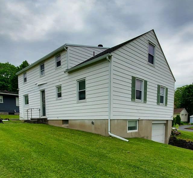 A large white house sits on top of a lush green hillside.