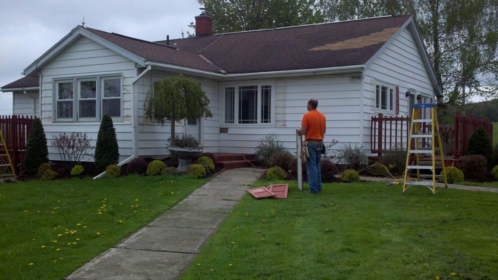 A man in an orange shirt is standing in front of a white house.