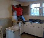 A man is hanging wallpaper on a wall in a kitchen.