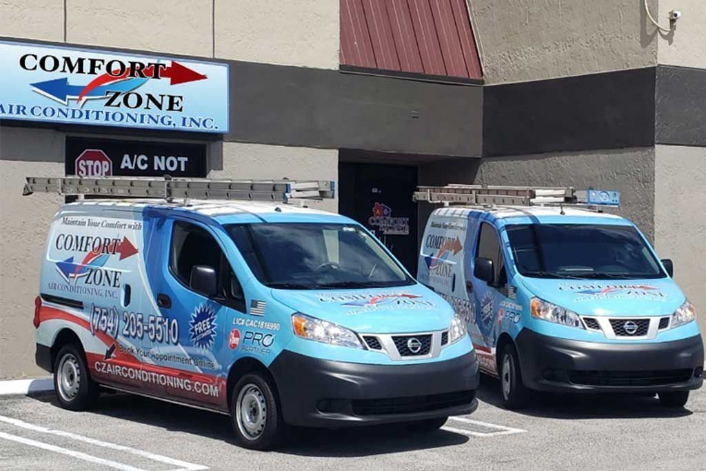Two blue Comfort Zone Airconditioning vans parked in front of a building with a sign.