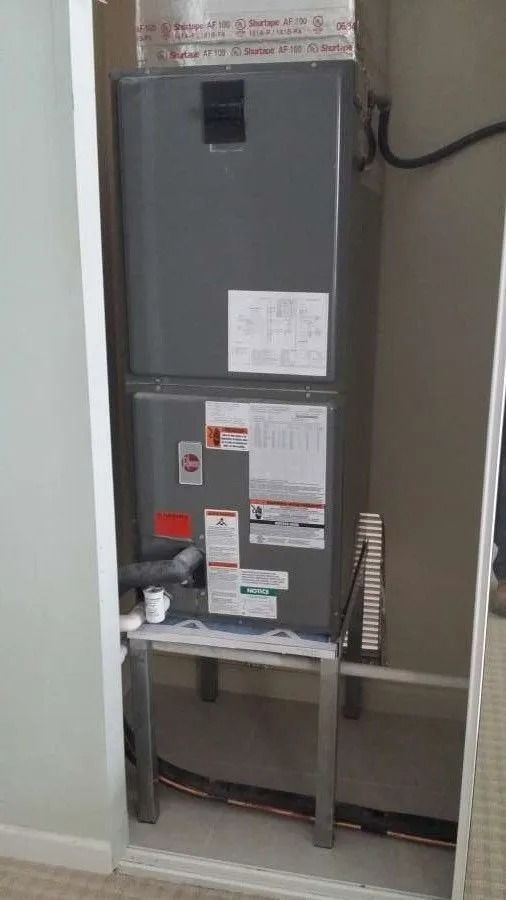 HVAC unit installed in a closet. Gray metal, with labels, white, and a silver stand.
