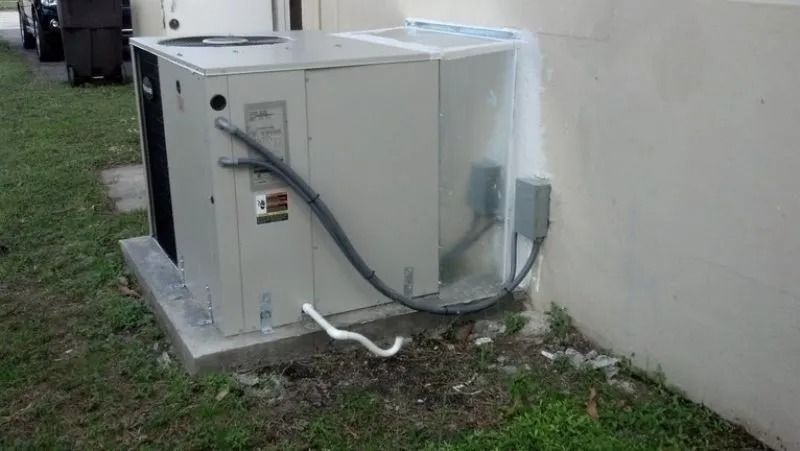 An outdoor air conditioning unit next to a light-colored wall and grass.