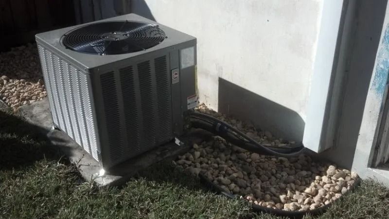 Air conditioning unit outside a building, on a concrete pad, surrounded by gravel and grass.