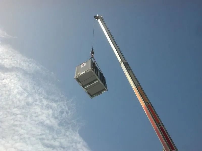 Crane lifting a rectangular container against a blue sky with light clouds.