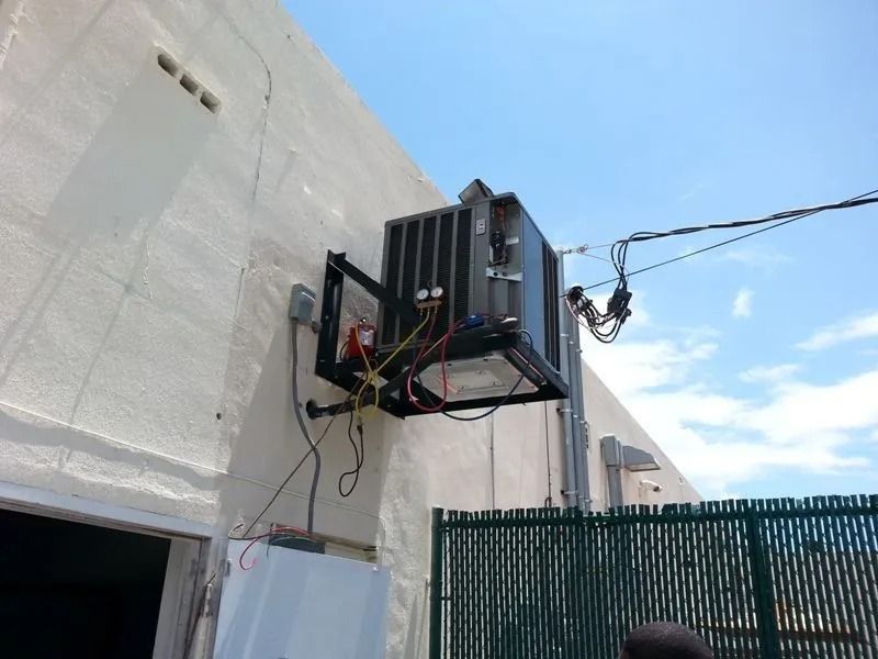 An air conditioning unit mounted on a building's exterior. Electrical wiring visible. Sunny day.