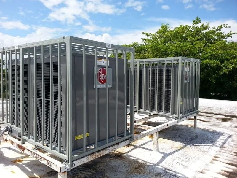 Two gray air conditioning units on a rooftop, each enclosed in a metal cage.