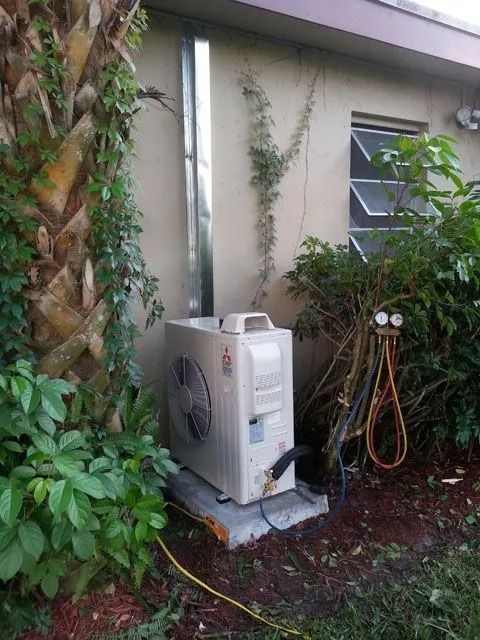 Air conditioning unit with a tall vent pipe, outdoor setting near a building with plants and gauges attached.