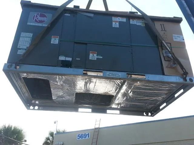 HVAC unit in shipping container being lifted by crane. Blue sky overhead.