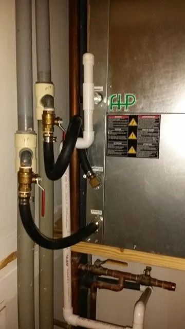 HVAC unit with connected pipes and valves. Black and gray pipes, copper lines, and a white drain line.