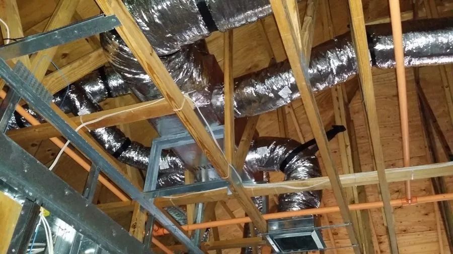 HVAC ductwork in an attic, with metallic flexible ducts against wooden beams and joists.