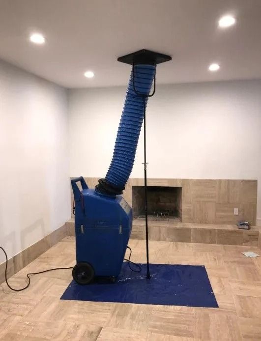 Blue dehumidifier with hose extending to ceiling in a room with a fireplace and tiled floor.