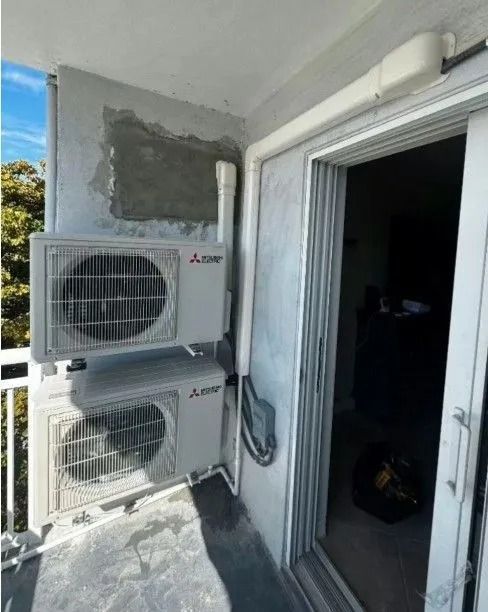 Two mounted Mitsubishi air conditioning units on a balcony next to a sliding glass door.
