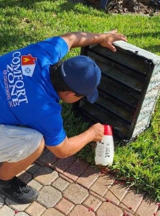 Man in blue shirt spraying a black vent on a patio, green grass background.