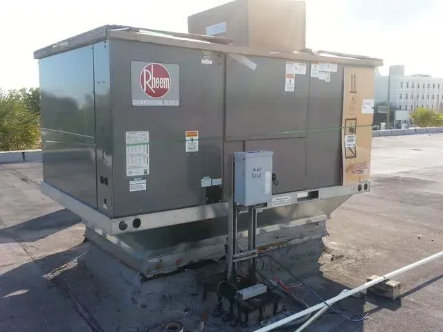 Rooftop Rheem HVAC unit on a flat roof. Gray metal box with a control box and wiring.