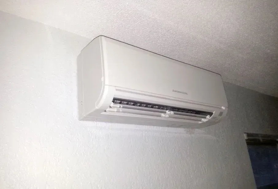 White wall-mounted air conditioning unit on a white wall; room interior.