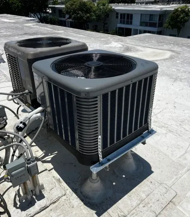 Two rooftop air conditioning units, grey, on a white roof, outdoors.