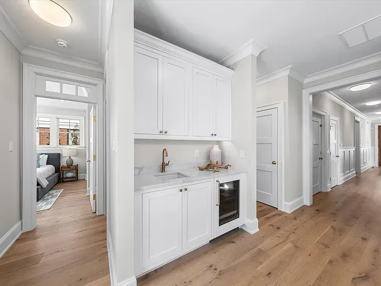 A hallway in a house with white cabinets and hardwood floors leading to a kitchen.