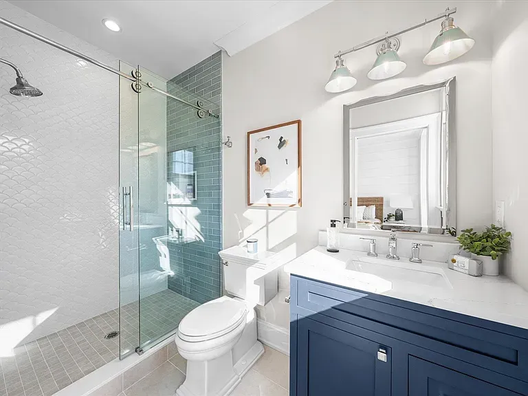 A bathroom with a toilet, sink, shower, and mirror.