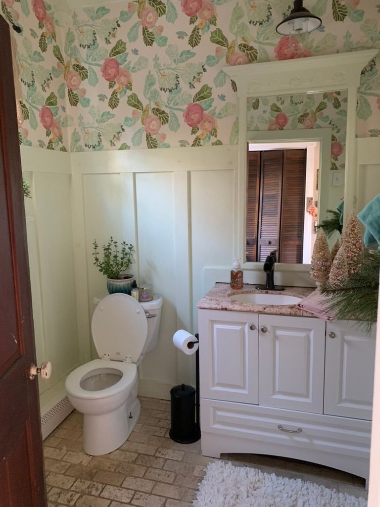 A bathroom with a toilet, sink, mirror, and floral wallpaper.